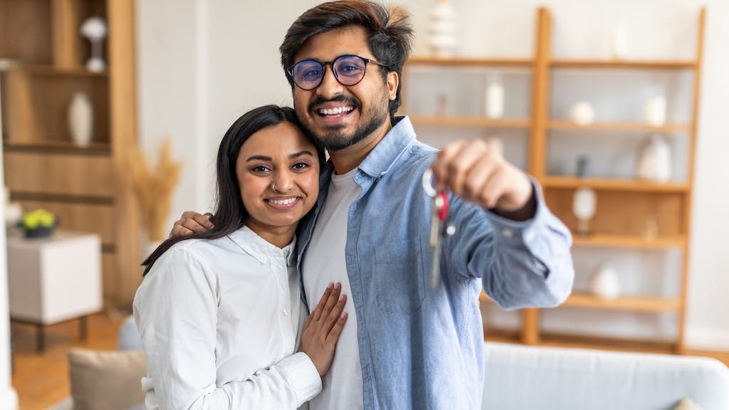 Millennial couple holds up keys to newly purchased home