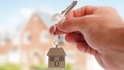 Foreign homebuyer holds up house key with home in background Foreign homebuyer holds up house key with home in background