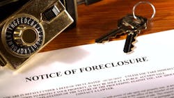 A notice of foreclosure sits on desk with house key and lock A notice of foreclosure sits on desk with house key and lock