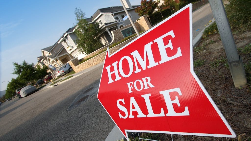 A red sign pointing to a home for sale