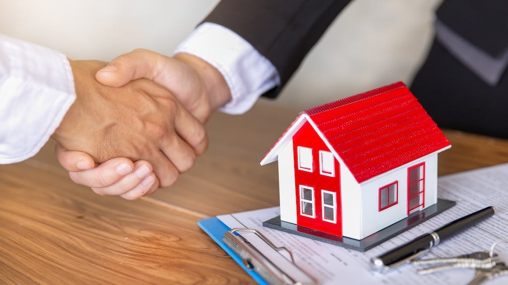 An investor shakes hands with a real estate agent after buying a home