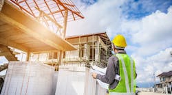 Construction worker stands at a jobsite looking over plans Construction worker stands at a jobsite looking over plans