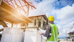 Construction worker stands at a jobsite looking over plans Construction worker stands at a jobsite looking over plans