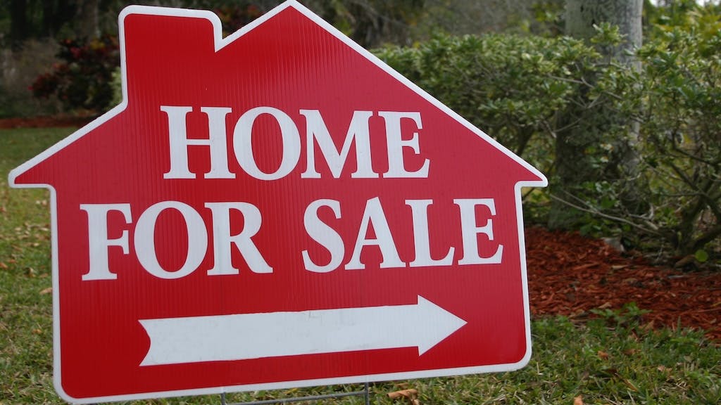 A red sign pointing to a home for sale