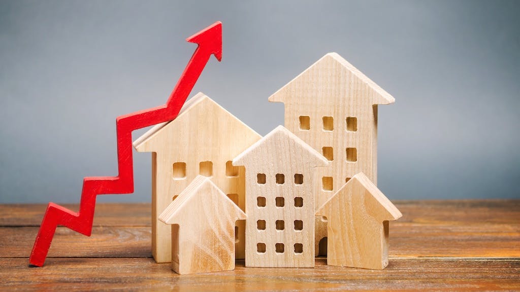 Wooden model homes with a red arrow pointing up, indicating price growth