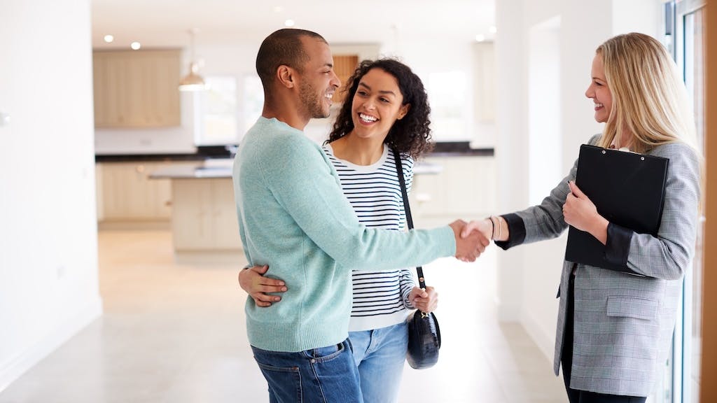 A couple shakes hands with a real estate agent while touring a home