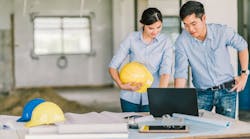 A man and a woman holding a hard hat looks over plans on a laptop at a construction site A man and a woman holding a hard hat looks over plans on a laptop at a construction site