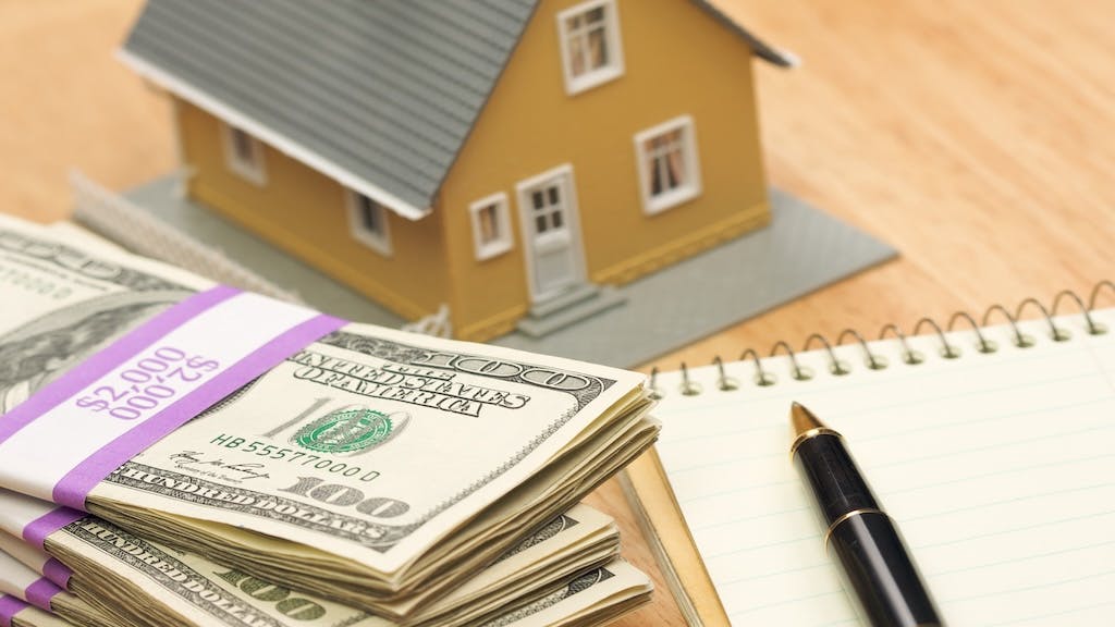 A stack of cash sitting next to a model home, indicating down payment money