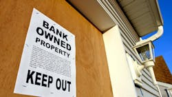 Boarded up home with a sign showing that it is bank-owned Boarded up home with a sign showing that it is bank-owned