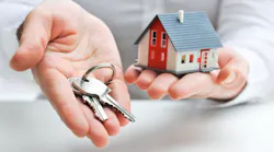 A hand holding out a key and a model home