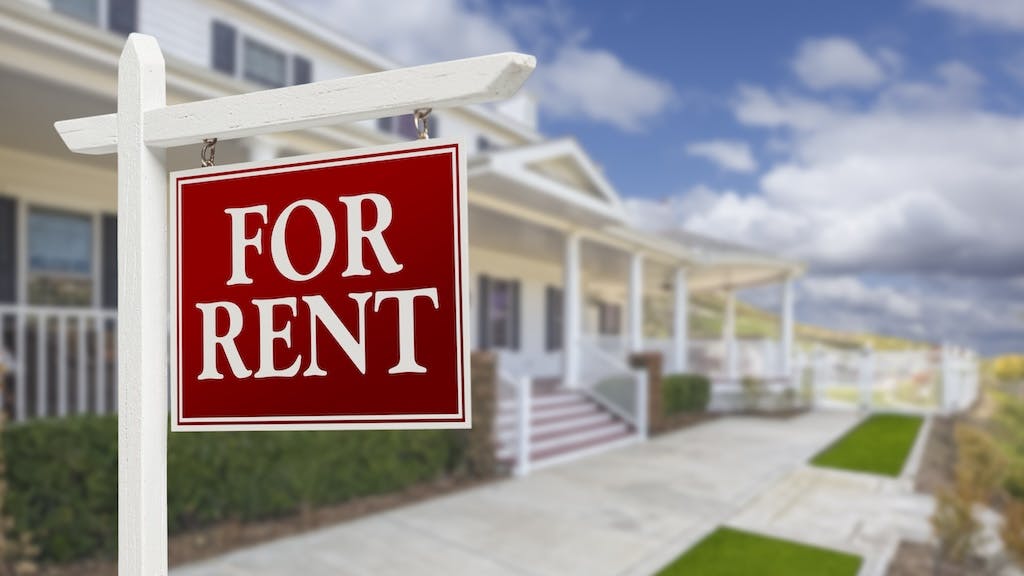 A 'For Rent' sign in front of a single-family home