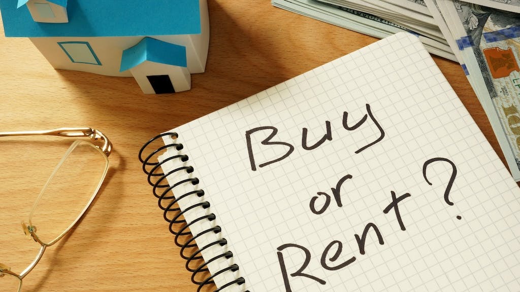 'Buy or Rent?' written on a notebook, next to a stack of cash and a model home