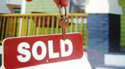 Homeowner holding house keys in front of a 'Sold' sign