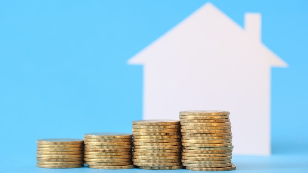 Stacks of coins in increasing order stand in front of a home, indicating equity