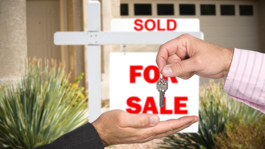 A homebuyer takes a key from real estate agent in front of a 'sold' sign