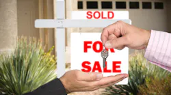 A homebuyer takes a key from real estate agent in front of a 'sold' sign