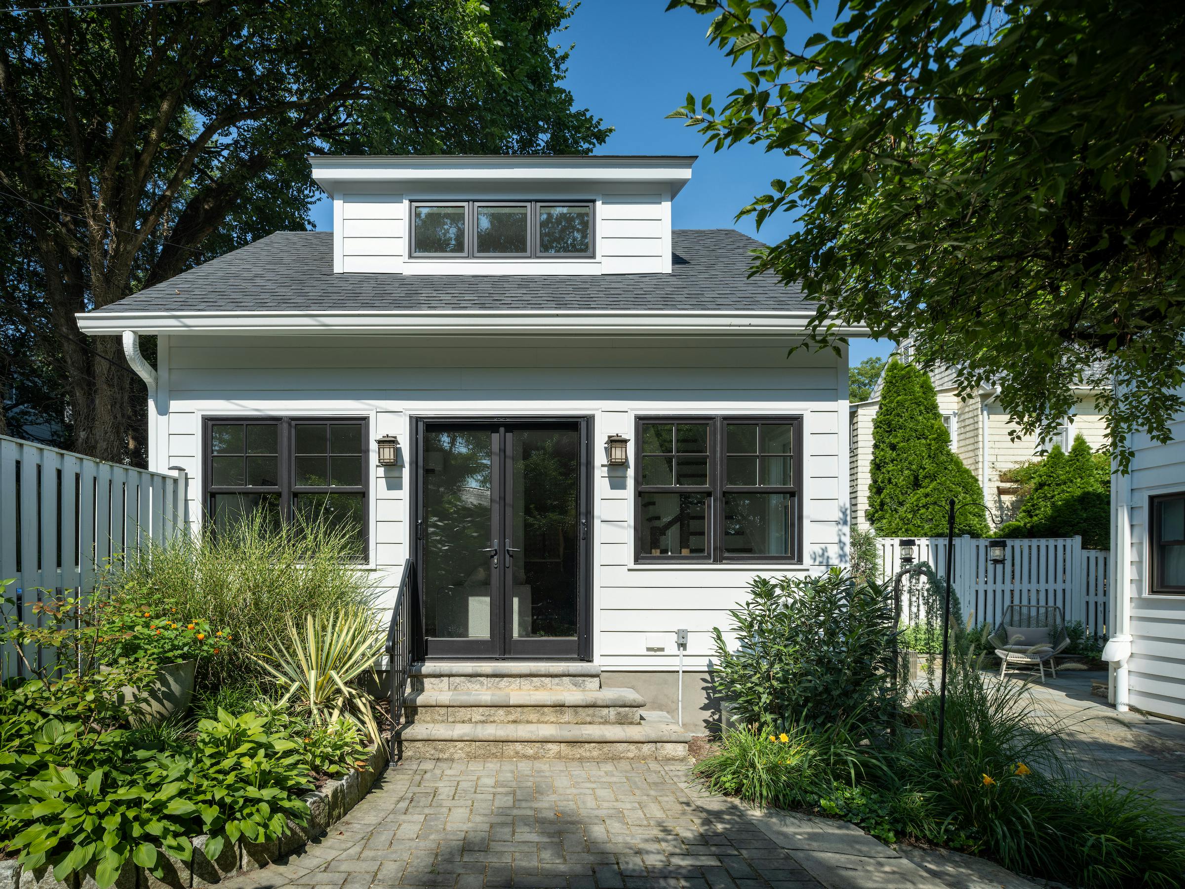The exterior of the finished conversion of a 1922 storage garage maintained the original's style and size, but extended the width of the existing dormer window to allow more natural light into the space.