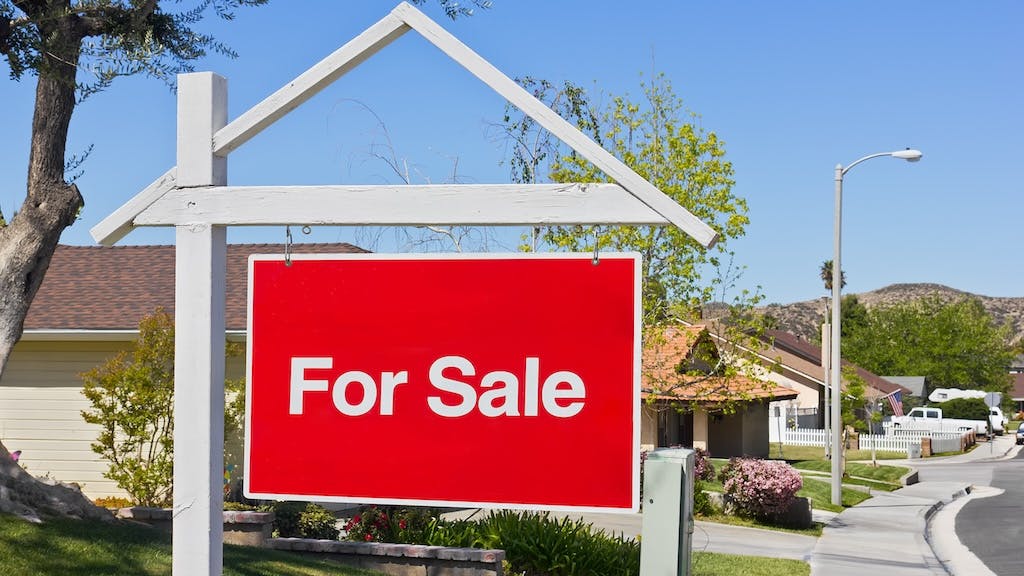 For sale sign in the front yard of a suburban home