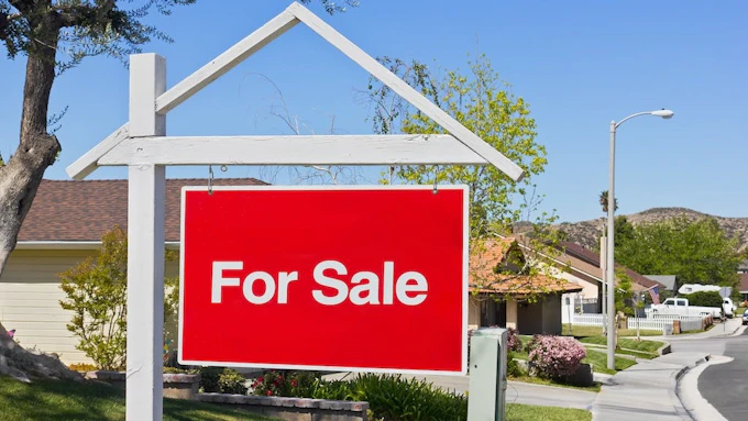 For sale sign in the front yard of a suburban home