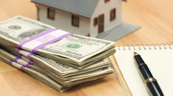 A stack of money next to a model home, representing a down payment